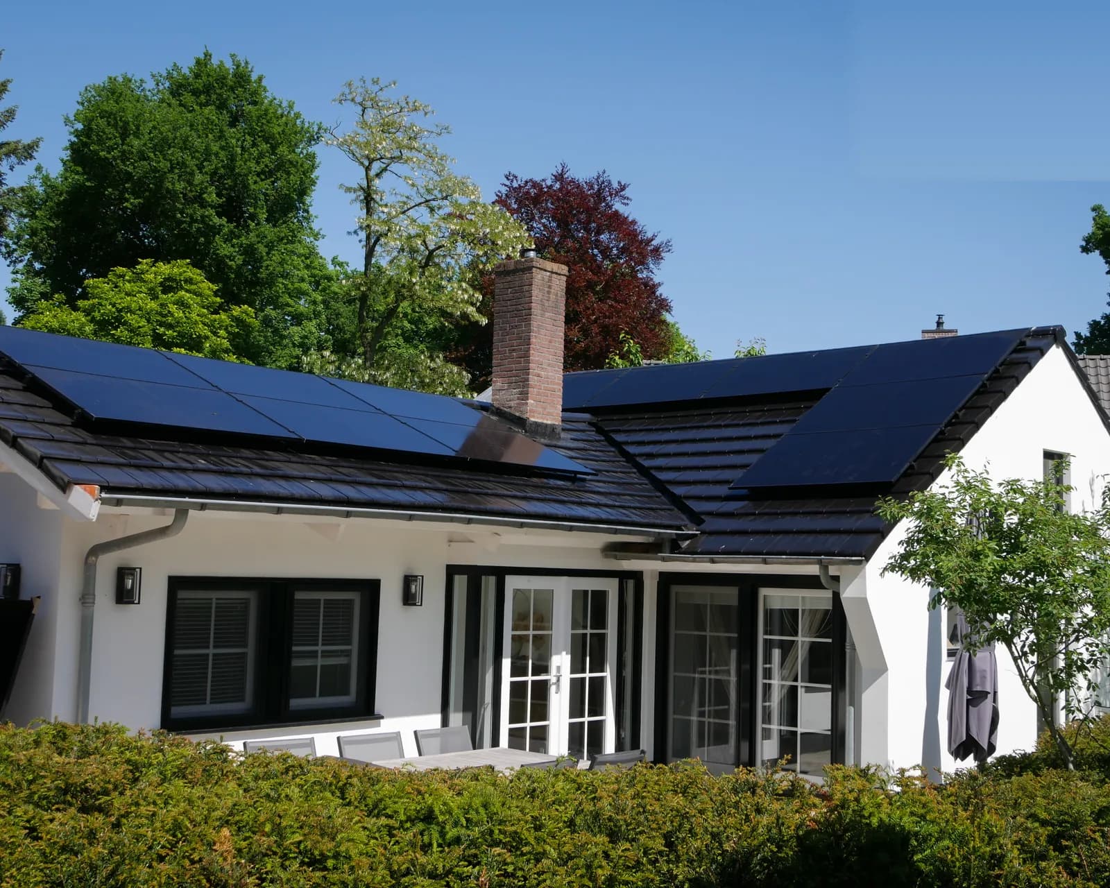 Witte woning met zonnepanelen op het dak en een groene tuin