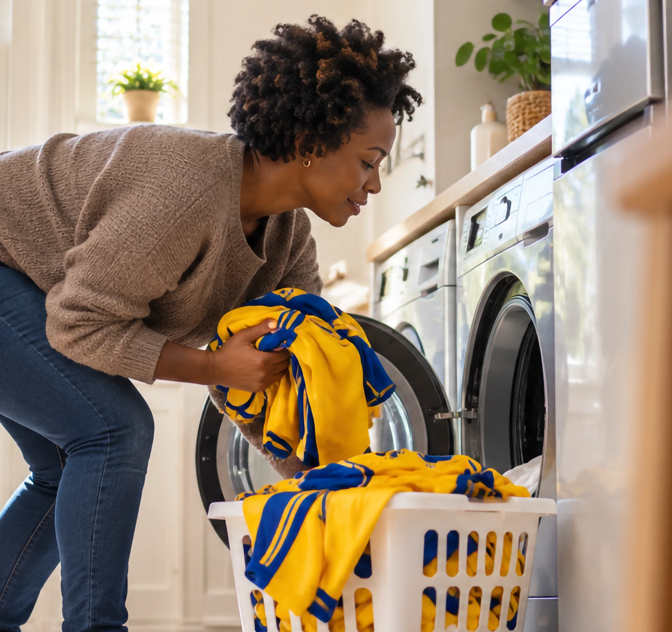 Vrouw haalt een geel-blauw voetbalshirt uit de wasmachine in een zonnige wasruimte